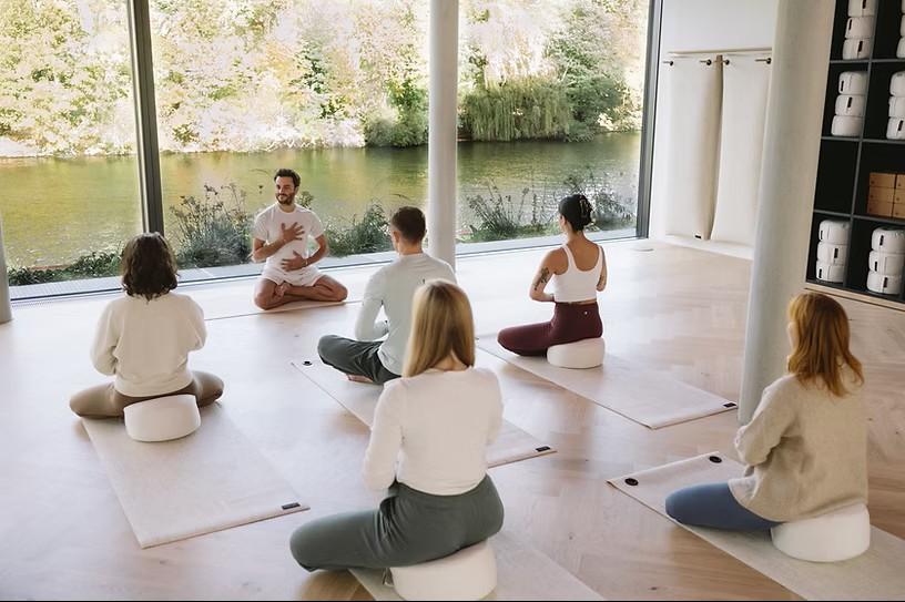 A small group sitting in meditation by a large window overlooking a river.